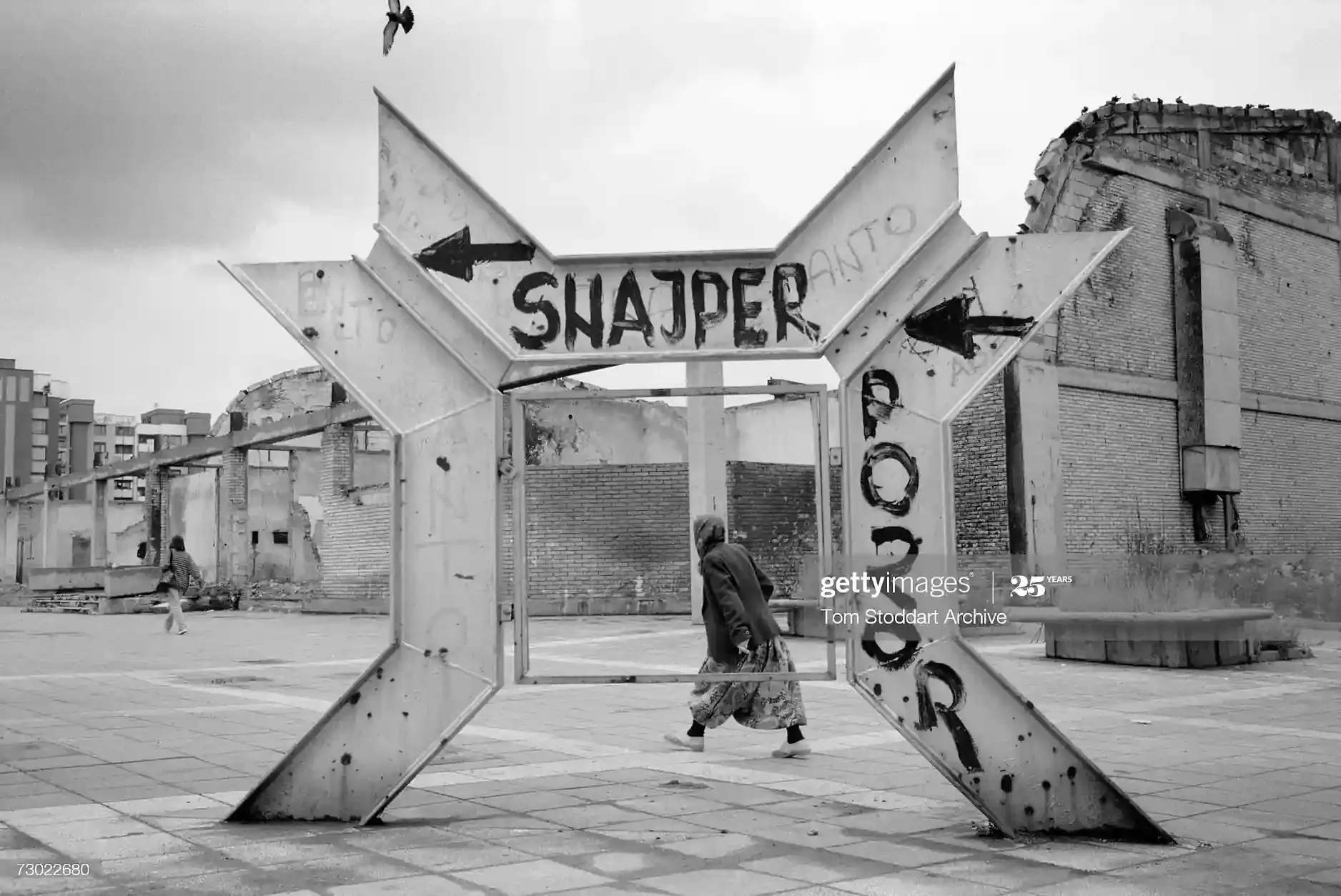 A woman walks past a sniper warning sign in Mojmilo, 1993